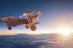 dichtbij omhoog van een wijnoogst houten speelgoed- vliegtuig, gehouden omhoog door een hand, vliegend bovenstaand de wolken in de lucht foto