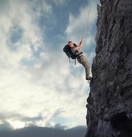 Mens klimt een hoog Gevaar berg met een touw foto