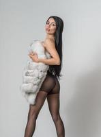 sensueel vrouw in zwart panty ,wit kort vacht en lang poten poseren uitdagend in voorkant van achtergrond. klassiek boudoir tafereel. studio erotisch foto. aantrekkelijk meisje met hoog hakken Aan hoog stoel foto