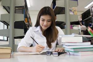 jonge mooie Aziatische student lachend tijdens het lezen in de bibliotheek foto