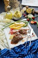 gegrilde steak en frietjes, met keukengerei op een witte plaat met groenten op donkere houten tafel foto