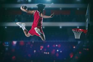 basketbal spel met een hoog springen speler naar maken een dichtslaan dunk naar de mand foto