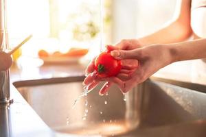 vrouw reinigt tomaten in de keuken in haar huis verlichte door de zon foto