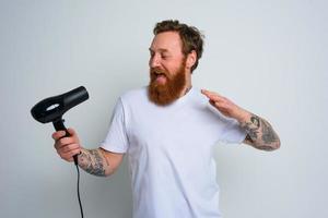 gelukkig Mens met baard gebruik haar- droger net zo microfoon en dansen foto