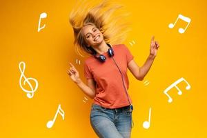blond meisje luistert naar muziek- met hoofdtelefoon. blij uitdrukking Aan geel achtergrond foto