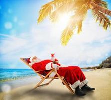 de kerstman claus ontspannende Aan een ligstoel in een tropisch strand foto