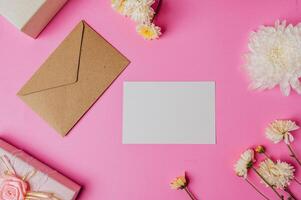 bruin envelop en kaart met geschenk doos Aan roze achtergrond versierd met bloemen foto