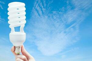 energie besparing concept, vrouw hand- Holding licht lamp Aan blauw lucht achtergrond, ideeën licht lamp in de hand- foto