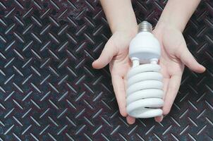 energie besparing concept, vrouw hand- Holding licht lamp Aan zink ijzer achtergrond, ideeën licht lamp in de hand- foto