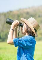 vrouw slijtage hoed en houden verrekijker in gras veld- foto