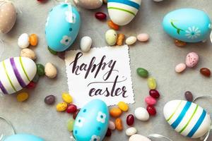 gelukkig Pasen-concept. voorbereiding op vakantie. paaseieren inscriptie happy easter letters candy chocolade-eieren en jellybean snoepjes op betonnen steen grijze achtergrond. plat lag bovenaanzicht kopieerruimte. foto