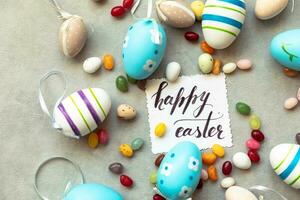 gelukkig Pasen-concept. voorbereiding op vakantie. paaseieren inscriptie happy easter letters candy chocolade-eieren en jellybean snoepjes op betonnen steen grijze achtergrond. plat lag bovenaanzicht kopieerruimte. foto