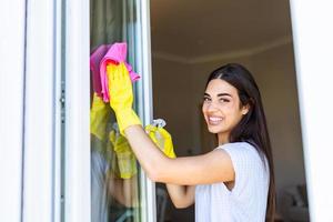 huiswerk en huishouding concept - gelukkig vrouw in handschoenen schoonmaak venster met vod en reiniger verstuiven Bij huis foto