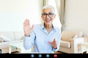 vrolijk volwassen vrouw hebben een video telefoontje van huis, online bedrijf concept. senior vrouw golvend foto
