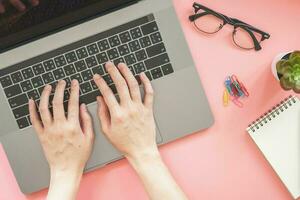 vrouw typen Aan laptop in roze pastel kleurrijk kantoor met accessoires foto
