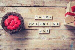 geschenk doos en rood hart in nest met houten tekst gelukkig Valentijn dag Aan hout tafel achtergrond. foto