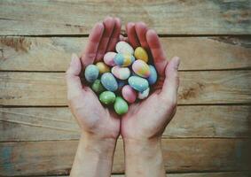 hand- vrouw Holding kleurrijk Pasen eieren Aan hout tafel achtergrond. foto