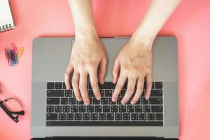 Dames typen Aan laptop in roze pastel kleurrijk kantoor met accessoires foto