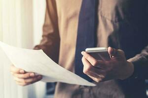 jong bedrijf Mens Holding papier en gebruik makend van smartphone in de kantoor met zonlicht. wijnoogst afgezwakt filter. foto