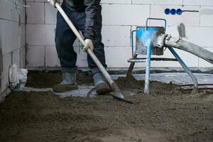 half droog verdieping dekvloer - een arbeider schoppen een bouw mengsel door een speciaal mouw voor cementeren en nivelleren Aan ondervloer verwarming pijpen. foto