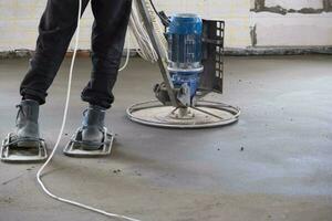 rammen en slijpen van half droog verdieping dekvloer door een machine met een roterend schijf voor nivellering. bouw van een beton verdieping in de huis, een meester met speciaal apparatuur. foto