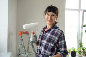 gelukkig vrouw in verf rol en wit verf voor muren in handen detailopname portret. bouw werk en kunstmatig reparaties in huis, muur schilderen, verven, afwerking werk met uw eigen handen foto