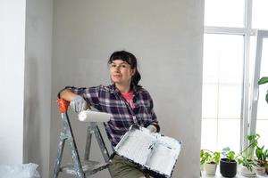 gelukkig vrouw in verf rol en wit verf voor muren in handen detailopname portret. bouw werk en kunstmatig reparaties in huis, muur schilderen, verven, afwerking werk met uw eigen handen foto