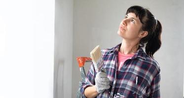 verbaasd vrouw in verf rol en wit verf voor muren in handen detailopname portret. bouw werk en kunstmatig reparaties in huis, muur schilderen, verven, afwerking werk met uw eigen handen foto