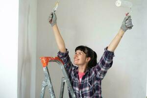 gelukkig vrouw in verf rol en wit verf voor muren in handen detailopname portret. bouw werk en kunstmatig reparaties in huis, muur schilderen, verven, afwerking werk met uw eigen handen foto