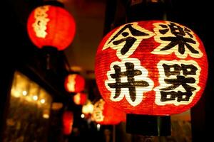 zwart Japans teksten Aan rood papier lantaarn hangende onder Japans restaurant dakrand Aan nacht tijd met wazig achtergrond. foto