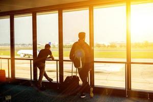 toerist mannen aan het wachten voor de lucht vlak in de luchthaven terminal lobby met zon en lens gloed en lucht vlak Aan rennen manier achtergrond. foto