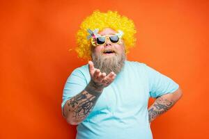 dik gelukkig Mens met baard, tatoeages en zonnebril heeft pret met de geel pruik foto