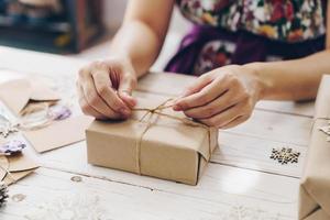 dichtbij omhoog van handen Holding omhulsel geschenk doos Aan houten tafel met Kerstmis decoratie. foto