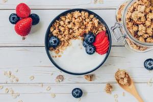 kom van muesli met yoghurt, vers bessen, aardbei Aan hout tafel. foto