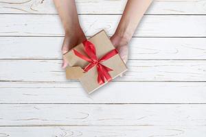 vrouw hand- Holding geschenk doos Aan hout plank en geschilderd in wit kleur met kopiëren ruimte. foto