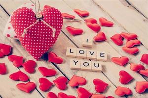 rood hart kleding stof en hout tekst van ik liefde u Aan houten tafel achtergrond. foto