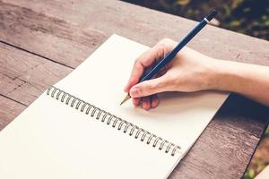 dichtbij omhoog hand- vrouw schrijven notitieboekje met potlood Aan hout tafel. wijnoogst afgezwakt filter. foto