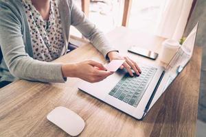 Aziatisch vrouw Holding credit kaart betalen voor boodschappen doen in computer laptop Aan houten tafel foto