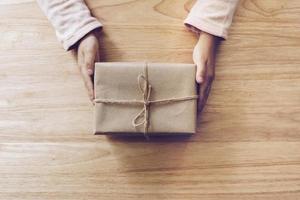 meisje hand- Holding geschenk doos Aan hout tafel achtergrond foto