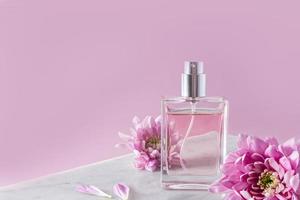 een chique fles van vrouwen parfum of toilet water Aan een wit marmeren podium met lila bloemen. voorkant visie. roze achtergrond. een kopiëren ruimte. foto