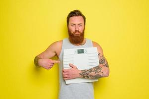 ongelukkig Mens met baard en tatoeages houdt een elektronisch balans foto