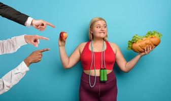 dik meisje is onbeslist naar eten een appel of een groot Sandwich. cyaan achtergrond foto