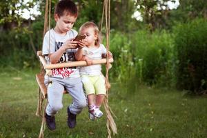 kinderen zittend Aan een schommel met telefoon foto