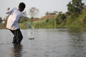 Aziatisch jongen is uitgeven zijn vrije tijd door duiken, zwemmen, het werpen rotsen en vangen vis in de rivier- gelukkig, hobby en geluk van kinderen concept, in beweging. foto