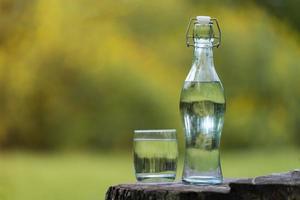 fles drinkwater en glas met natuurlijke achtergrond foto