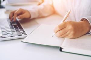 vrouw schrijven in een planner-notebook tijdens het gebruik van laptop thuis foto