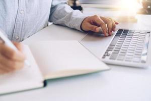 vrouw schrijven in een planner-notebook tijdens het gebruik van laptop thuis foto