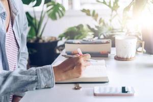 vrouw schrijven in een planner-notebook tijdens het gebruik van laptop thuis foto