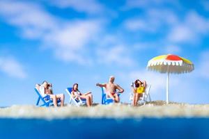 miniatuurmensen die op het strand met een blauwe hemelachtergrond zonnebaden, zomerconcept foto
