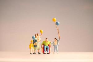 miniatuurmensen tonen een positief gezin dat voor hun gehandicapte vader zorgt foto